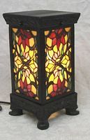 Four-sided stained glass lamp powered on, showing colorful floral stained glass panels with black metal frame and decorative base.
