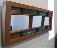 Side angle view of rectangular wood-framed mirror with green stained glass panels inset along the frame and separating mirror sections.