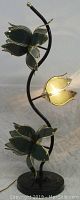 Front view of the lamp showing 3 flower-shaped lights off, with black metal stand curved with gold accents.