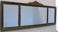 Front view of the entire tri-panel mirror with gilt wood frame hanging on a wall.