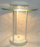 Front view of the lamp illuminated showing white base, glass shade, and perforated metallic top diffuser.