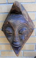 Front angled view of carved wooden mask showing facial features and geometric headdress pattern