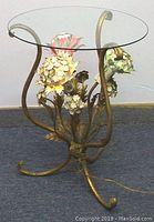 Full side view showing metal lamp base with three flower-shaped lamp shades illuminated in different colored bulbs and the round glass tabletop on top.
