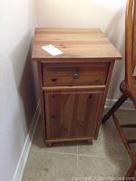 Front view of a small wooden telephone table with drawer and storage cabinet door underneath.