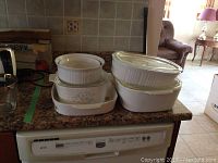Wide view of six CorningWare containers on granite countertop showing various sizes and three glass lids