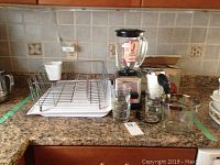 Photo showing the lot including Hamilton Beach blender with glass jar and lid, Sunbeam hand mixer, five RCMP glass tumblers, and metal dish drying rack on a kitchen counter.
