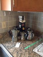 Photo showing all five stovetop coffee percolators and the whipped cream maker with charger boxes on kitchen countertop.