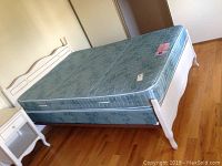 Photo of assembled double bed with wood headboard and footboard, mattress and box spring placed on wood floor.