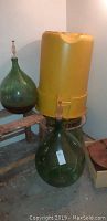 Overview of two green glass carboys with plastic airlocks and yellow metal-encased fruit press on stand