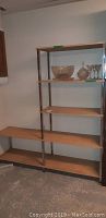 Full view of the two-part shelf with chrome frame and wood shelves, empty except for some glassware on upper shelves in the taller section.