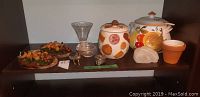 Two ceramic canisters with lids featuring fruit decor on a shelf with other decorative items including a glass vase, small containers, a faux agate stone, and a small flower pot.