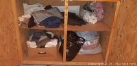 Fabric remnants and miscellaneous fabrics on two levels of a wooden shelf. Includes folded and bagged fabrics.