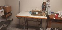 Wide angle showing Singer 807 sewing machine on white topped table against wall with nearby shelving and other items.