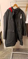 Front view of a long dark-colored men's parka with red hood lining hanging on a rack.