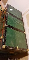 Photo showing top and side of large green storage chest with visible scratches and metal corner protectors.