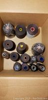 Top view showing a total of twelve large and medium spools predominantly in dark brown and black colors in a cardboard box.