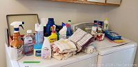 Photo showing various bottles of cleaning and laundry supplies alongside folded tea towels on top of laundry machines.