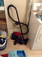 Bissell canister vacuum with hose and attachments placed near laundry area.