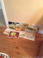 Photo showing eight original 10x12 paintings loosely arranged on hardwood floor against wall.