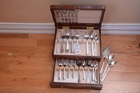 View of entire flatware set including forks, spoons, knives, and serving utensils inside wooden flatware chest with two drawers.