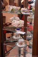 Display shelf showing decorative porcelain bowl with lid and Royal Crown mug and saucer with classical figure designs.