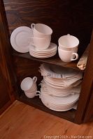 Full view of the stacked dishes and cups inside a wooden cabinet shelf.