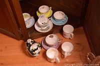 Overall view of 6 tea cup and saucer sets and 3 mugs with floral patterns on hardwood floor