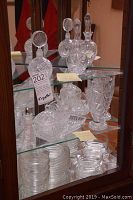 Crystal lot displayed in a glass cabinet; includes a tall vase, two bottles with stoppers, small bowls and plates, and a tray all with cut Pinwheel crystal design patterns.