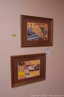 Two framed watercolor art pieces hanging on wall, featuring autumn and boathouse scenes