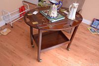 Photo showing the closed wooden folding serving cart with various items on top, including decorative ceramics and books, highlighting its flat surface and castor wheels.