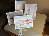 Four unframed original watercolor paintings displayed on a table showing coastal and boat scenes.