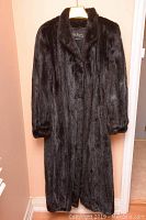 Full-length front view of black mink fur coat hanging on hanger