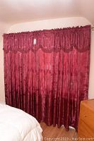 Full view of three red curtains with valance on gold metal rod
