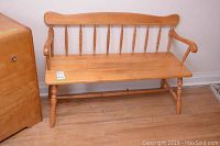 Full view of the wooden bench showing the seat, backrest with spindles, armrests, and turned legs on a hardwood floor.