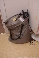 Roots branded gray storage bag filled with air bed, showing carrying handles and some cords attached.