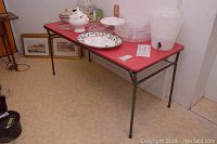 Photo of the resin folding table in use with items on top, showing red surface and black metal legs.