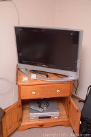 Samsung 26-inch TV shown on top of wooden cabinet with remote on top and Panasonic DVD player inside cabinet.