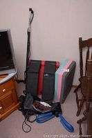Black EZGYM system bag with resistance cables, pink/blue/gray foam stepper block and blue shaped resistance bar leaning against the wall indoors