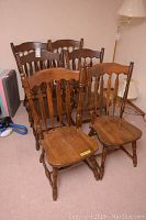Photo showing the full set of six wooden chairs grouped together in a room with visible wear and scratches.