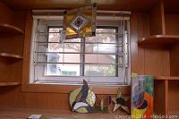 View of four stained glass pieces set on a wood shelf in front of a window: oval bird, butterfly, star bird, and tall rectangular piece