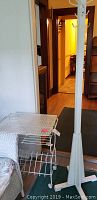 Photo showing the rolling metal magazine rack with mesh top and shelves next to the white painted wood coat rack.