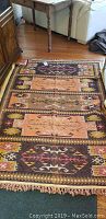Full view of the vintage area rug laid on hardwood floor, showing overall pattern, size and fringe details.