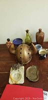 Photo showing Viking brass helmet, pottery and glass jugs, ceramic and decorative metal pieces on wooden surface