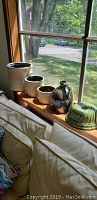 Full view of all items: four stoneware canisters on wooden window sill, dark glazed jug, green decorative mold beside canisters