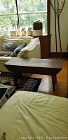 Side angle showing the bench placed near sofa with pillows and a small cabinet behind it.