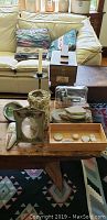 Photo showing antique iron candlestand, Kiwi Shoe Valet box, artistic rock stack, vintage iron picture frame, clam shell ashtray, small wood box and stone artifacts arranged on a wooden table.