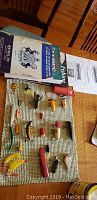 Image showing various fishing lures arranged on a mat, with fishing books placed nearby on a table.