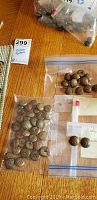 Plastic bags containing multiple vintage brass buttons arranged on a wooden surface with a label 'Vintage Buttons' and lot number visible.
