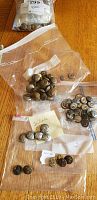 Overview of multiple ziplock bags containing vintage brass and metal buttons on wooden table surface