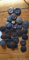 Photo showing entire collection of around thirty vintage buttons with American eagle motifs spread on a wooden surface, various sizes and metal finishes.